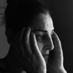 A dramatic black and white portrait of a woman looking thoughtful, holding her face.