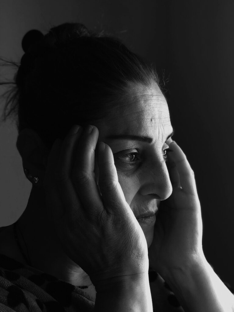 A dramatic black and white portrait of a woman looking thoughtful, holding her face.