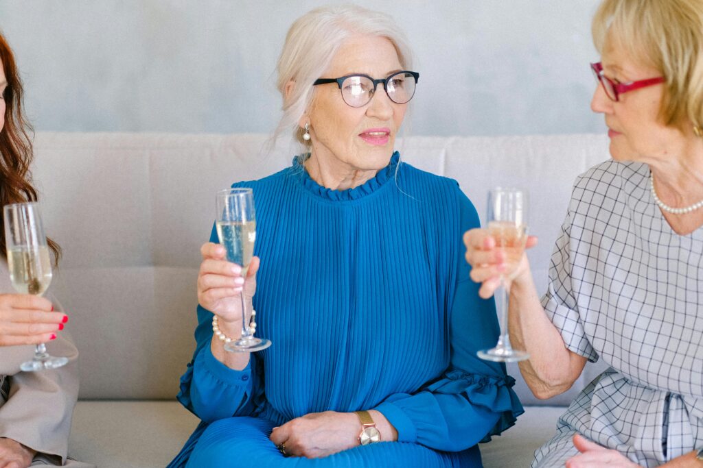 Group of aged women with glasses of crystal champagne chatting and looking at each other while congratulating each other