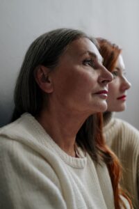 A portrait of a mature and young woman in side profile, wearing knitted sweaters indoors.