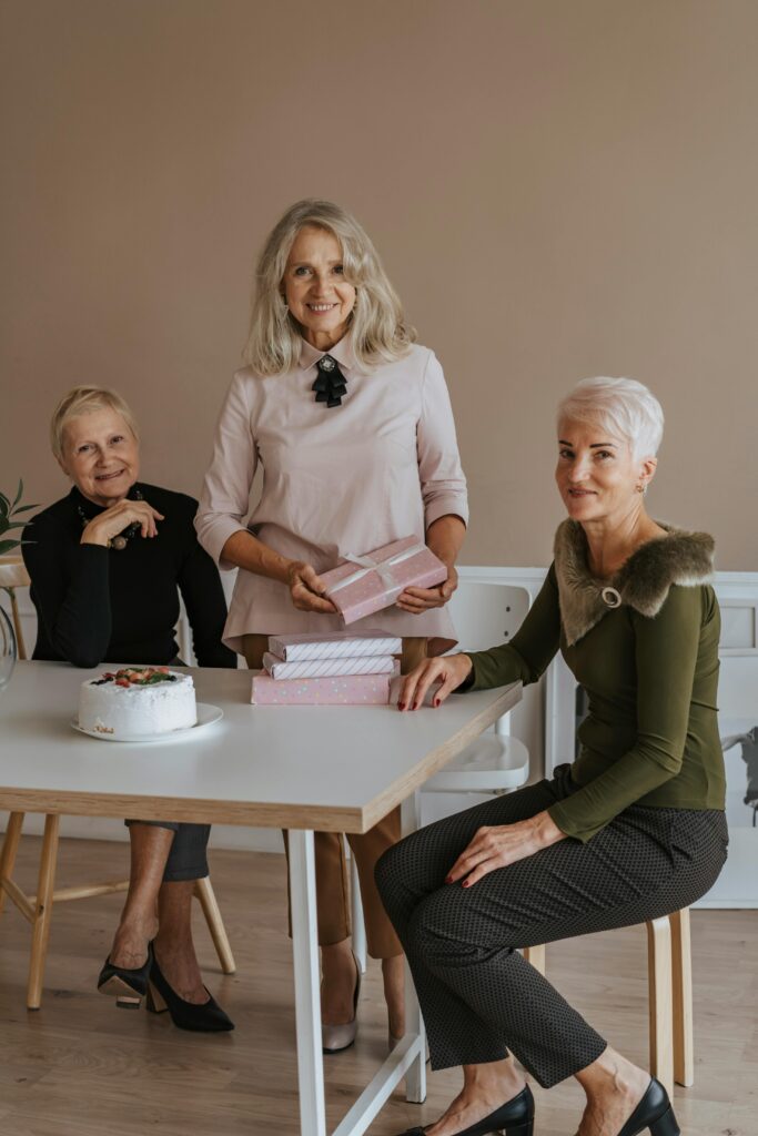 pexels-photo-5729092-5729092 Three senior women celebrating with gifts and a cake, enjoying a joyful gathering indoors.