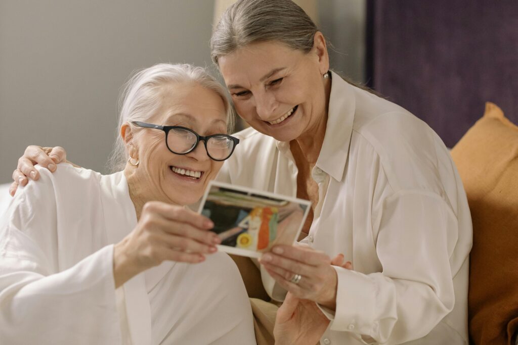 Two elderly women smiling and enjoying old photos, capturing heartfelt memories indoors.