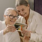 Two elderly women smiling and enjoying old photos, capturing heartfelt memories indoors.