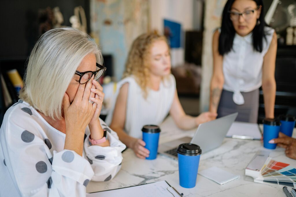 Office scene with women in a meeting, highlighting stress and teamwork dynamics.