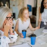 Office scene with women in a meeting, highlighting stress and teamwork dynamics.